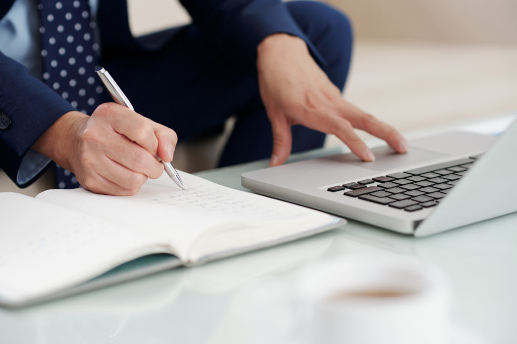 Businessman working on laptop and taking notes in his planner, selective focus